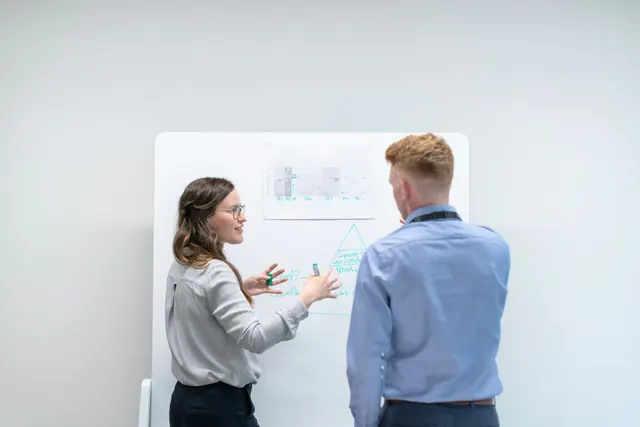 Deux collègues discutent de données présentées au tableau.